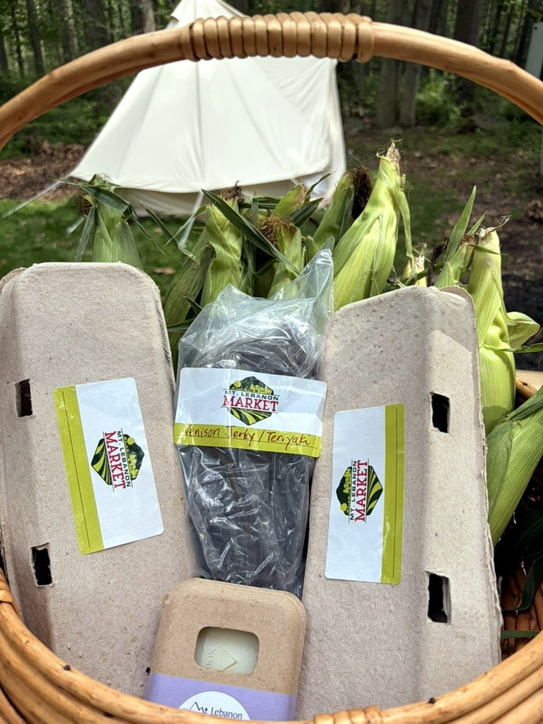 Basket of Mt. Lebanon Market eggs, venison jerky, handmade soap, and fresh corn in front of a canvas glamping tent