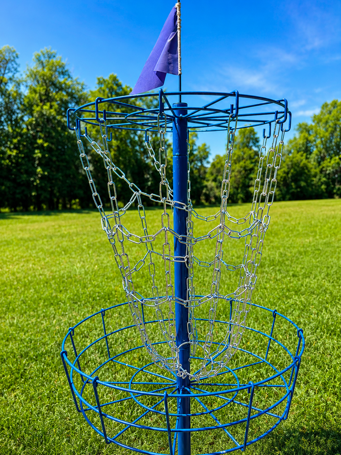 Blue disc golf basket with a purple flag in an open grassy field
